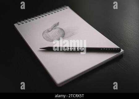 An apple pencil drawing in a notebook and a pencil on a black table. Learning to draw a concept. Stock Photo
