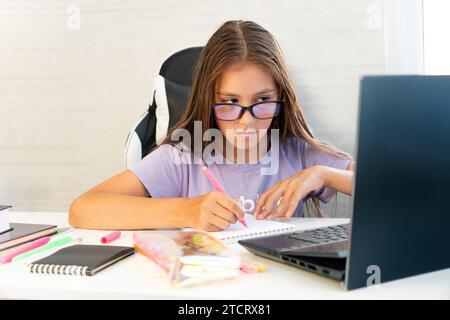 Primary school Student child writing in book using laptop. Distance learning online education. Schoolboy girl studying at home with digital tablet com Stock Photo