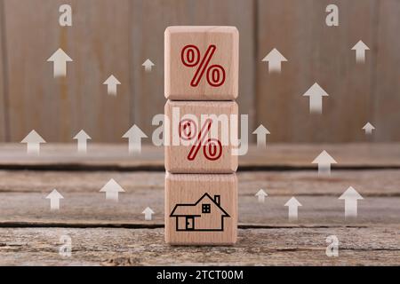 Mortgage rate rising illustrated by upward arrows and percent signs. Cubes with house icon on wooden table Stock Photo