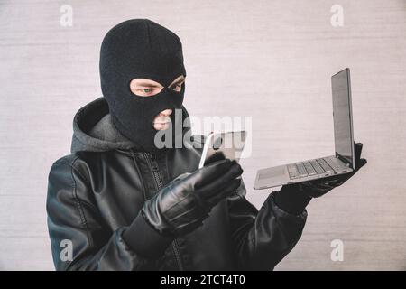 a hacker thief uses a smartphone and laptop to steal money over the Internet. Criminal concept. Thief on a white background with a laptop Stock Photo