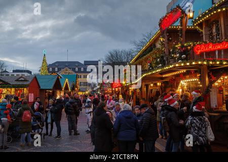 Bonn, Germany - Dec 6, 2023: Twilight view of a bustling Christmas market with festive lights, decorated stalls, and holiday shoppers. Stock Photo