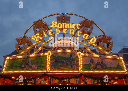 Bonn, Germany - Dec 6, 2023: Illuminated carousel sign 'Bonner Riesenrad' meaning 'Bonn ferris wheel' at dusk with festive lights and painted decorati Stock Photo