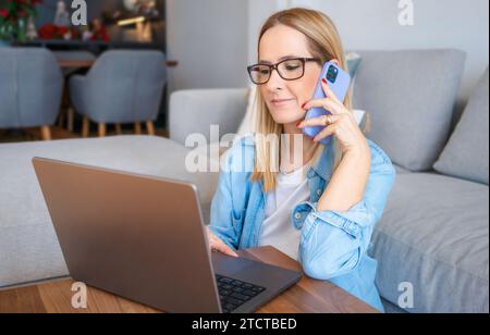 Happy young woman using laptop while working remotely from home in living room Stock Photo