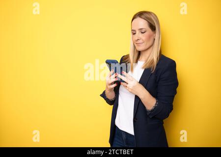 Young business woman using smartphone on yellow studio background Stock Photo