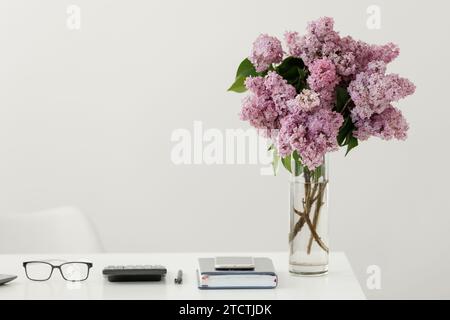 Business concept. Light work place of accountant at office with desk table, laptop, financial documents folder calculator, eyeglasses, smartphone, pen and big green houseplant. Copy space on wall. Stock Photo