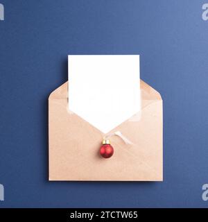 Kraft paper envelope with white card and Christmas decoration on dark blue background, top view. Stock Photo
