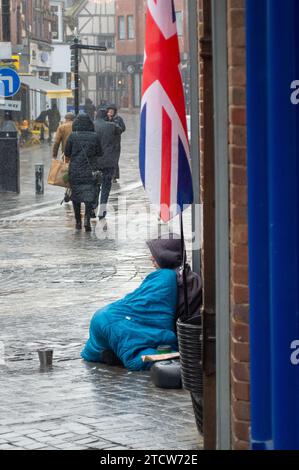 Windsor, UK. 14th December, 2023. Reece, a man who has been made homeless following the death of his father sits on the cold floor in the rain outside a shop in affluent Windsor, Berkshire hoping for passers by to give him some coins. Shelter Chief executive Polly Neate has told Sky News that "Homelessness is on nobody's Christmas list, but 309,000 people will spend this time of year in a tiny hostel room or freezing in a doorway". Credit: Maureen McLean/Ģ����ý Live News Stock Photo