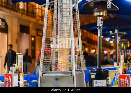 A burning gas flame heater warms tables at a sidewalk cafe at night in the touristic main shopping and dining street of Rua Agusta in Lisbon, Portugal Stock Photo
