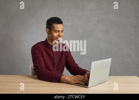 Positive african american programmer creates a new program and encodes while sitting at a laptop. Stock Photo