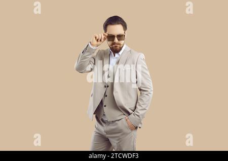 Handsome young man in formal suit and cool sunglasses posing on beige studio background Stock Photo
