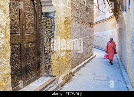 Beautiful carved wooden door and Muslim woman wearing djellaba / jillaba and hijab in alley of medina in the city Fes / Fez, Fez-Meknes, Morocco Stock Photo