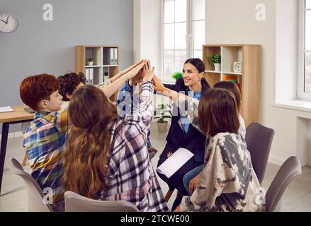 Happy junior school students and teacher giving high five together in classroom Stock Photo