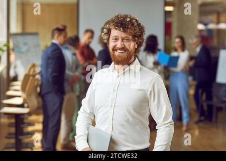 Happy bearded young business man looking at the camera and smiling in the office. Stock Photo