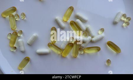 different capsules with vitamins on a white plate close-up top view, background on the theme of taking medications and nutritional supplements Stock Photo