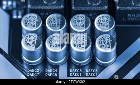 Closeup a group of aluminum electrolytic capacitors on PCB detail in blue tone. Condensers or inductors electronic components on printed circuit board. Stock Photo