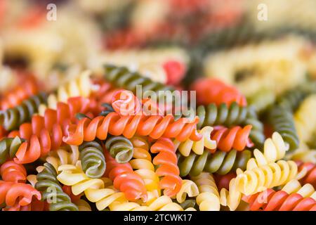 Closeup of colored spiral twisted fusilli pasta on pile with blurred background. Side view a heap of dry uncooked yellow, red and green eggless rotini. Stock Photo