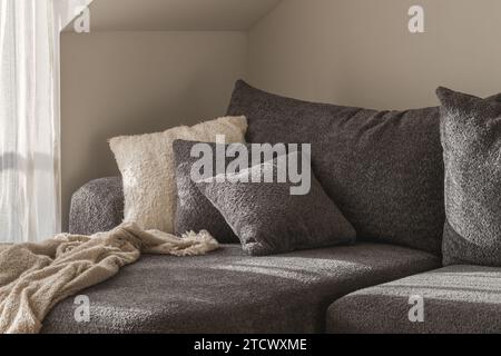 White and grey textured decorative pillows, cozy knitted blanket on a  dark grey sofa. Wabi-sabi interior details for decoration Stock Photo