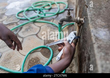 Close-up of the hands of an African plumber fixing the outside tap. Stock Photo