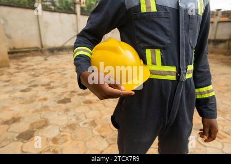 Faceless close-up of a technician dressed in his work outfit holding his yellow helmet. Stock Photo