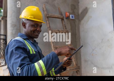 Smiling African electrician holds up his tablet at work. Electricity concept. Stock Photo