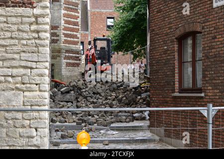 Small excavator stands on a pile of cobblestone rubble in a small alley blocked by steel fences in the city centre of Antwerp Stock Photo