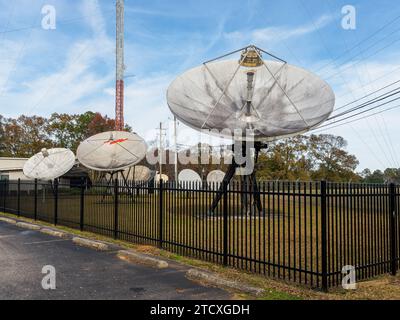 Large satellite dishes lined up under a tall television broadcasting tower or T.V. tower antenna in Montgomery Alabama, USA. Stock Photo