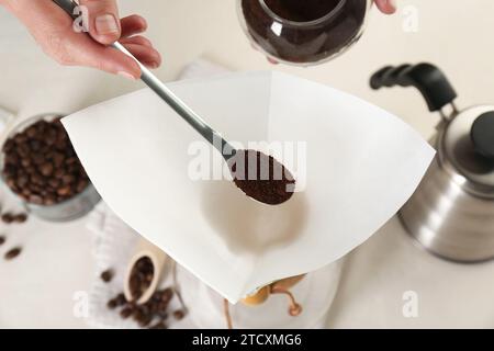 Making drip coffee. Woman adding ground coffee into paper filter at white table, closeup Stock Photo