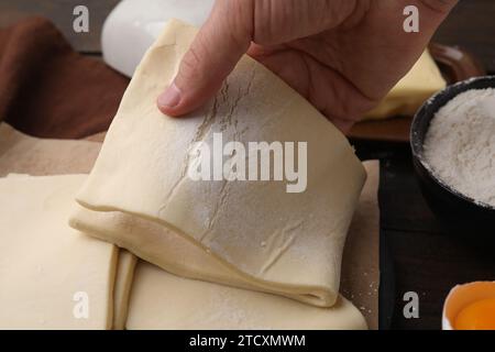 Man holding raw puff pastry dough at wooden table, closeup Stock Photo