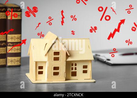 Mortgage rate rising illustrated by upward arrows and percent signs. House model on light gray table Stock Photo