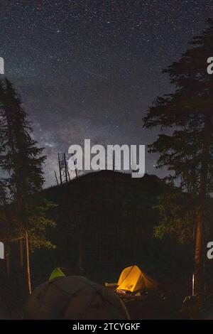 Illuminated tents nestle under a star-filled sky, offering a peaceful night in the backcountry of Rocky Mountain National Park. Stock Photo