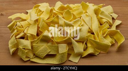 Traditional uncooked Italian Pappardelle isolated on wooden table. Stock Photo