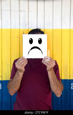Man with sad emoticon on a coloured wooden background Stock Photo