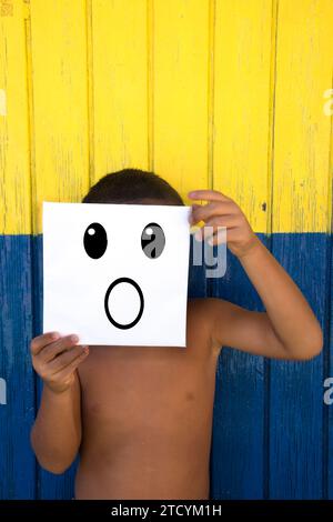 Boy with surprise emoticon on a coloured wooden background Stock Photo