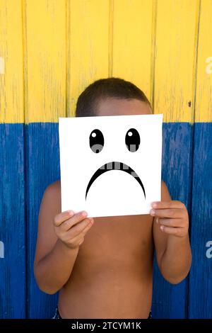 Boy with sad emoticon on a coloured wooden background Stock Photo