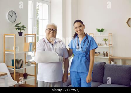 Young doctor and happy senior patient with broken arm standing together and smiling Stock Photo