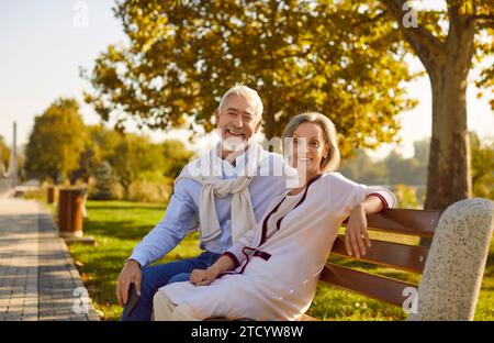 Portrait of happy married senior couple sitting on bench in beautiful green summer park Stock Photo
