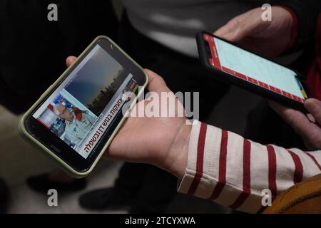 People watch news bulletin on a smartphone after rocket attack from Gaza as they take cover in a shelter at Ichilov Hospital which treated released hostages and continue to receive and treat wounded soldiers as the war with Hamas continues on December 11, 2023 in Tel Aviv, Israel. It has been more than two months since the Oct. 7 attacks by Hamas that prompted Israel's retaliatory air and ground campaign in the Gaza Strip. Stock Photo