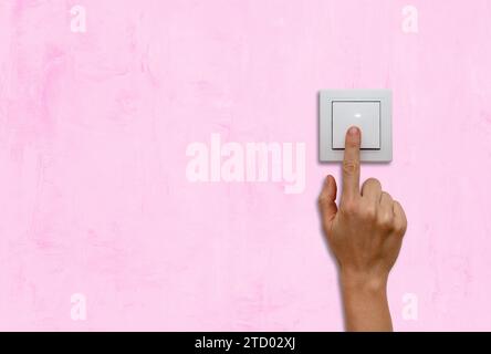 Female finger on light switch on pink coloured wall close up. Stock Photo