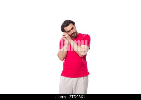 young brutal black-haired man dressed in a red corporate t-shirt on a white background Stock Photo