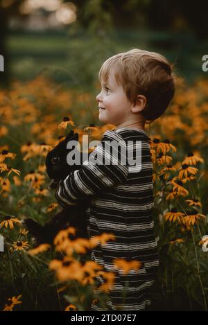 boy holding black fluffy bunny in flowers Stock Photo