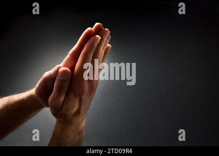 Praying man with hands with palms together contrasted with beam of light on dark isolated gradient background. Top elevated view. Stock Photo
