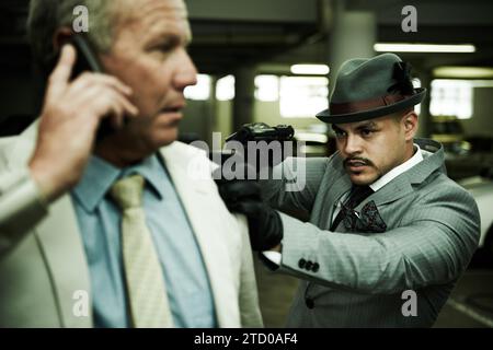 Man, parking lot and criminal with gun for crime, robbery or abduction with horror, mafia and negotiation on a phone call. Corporate boss, manager or Stock Photo