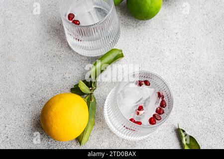 A sophisticated gin tonic cocktail with lemon and red berries, served on a textured surface with fresh citrus in view. Stock Photo