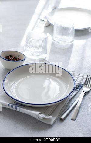 A stylish dining setup featuring a white plate with blue rim, cutlery, and glassware arranged on a textured tablecloth. Stock Photo