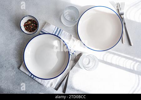 Modern dinnerware arrangement on a marble surface, including white plates with blue trim, silverware, and a striped napkin, creating an elegant table Stock Photo