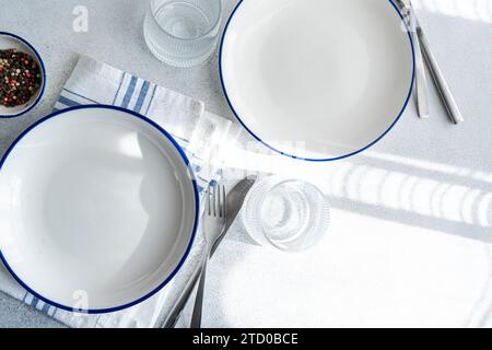 An overhead view of a sophisticated table setting featuring white plates with blue rims, silver cutlery, and glassware on a linen tablecloth. Stock Photo