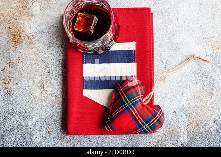 A red hardcover book with a plaid fabric heart and a vintage glass on top, representing a love of vintage literature. Stock Photo