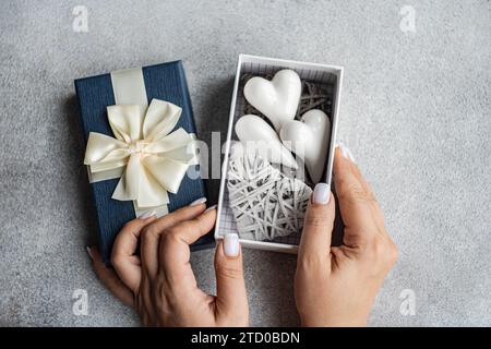 Hands gently holding an open gift box revealing white heart ornaments against a delicate lace background. Stock Photo