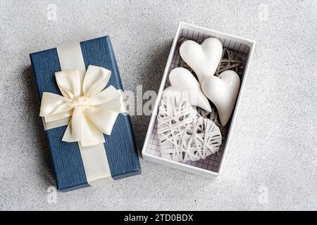 A blue gift box with a cream ribbon, opened to show white heart ornaments on a lace background Stock Photo