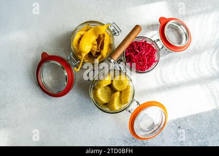 Sealed jars of fermented vegetables including cabbage with beetroot, spicy peppers, and pickled cucumbers on a light background. Stock Photo